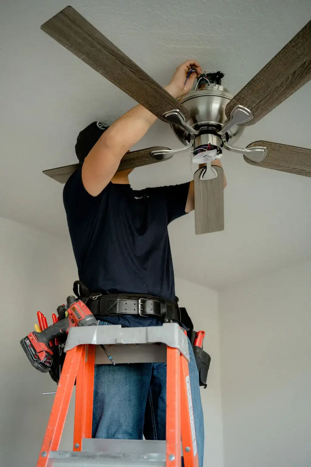 Electrician on an orange ladder installing a ceiling fan