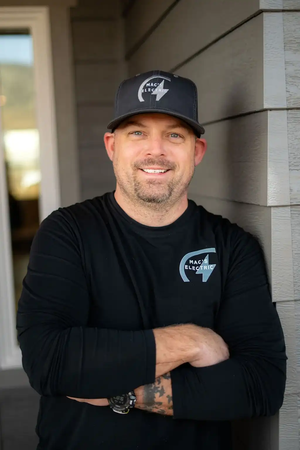 MAC's Electric electrician in a logo cap and shirt, smiling outside a home